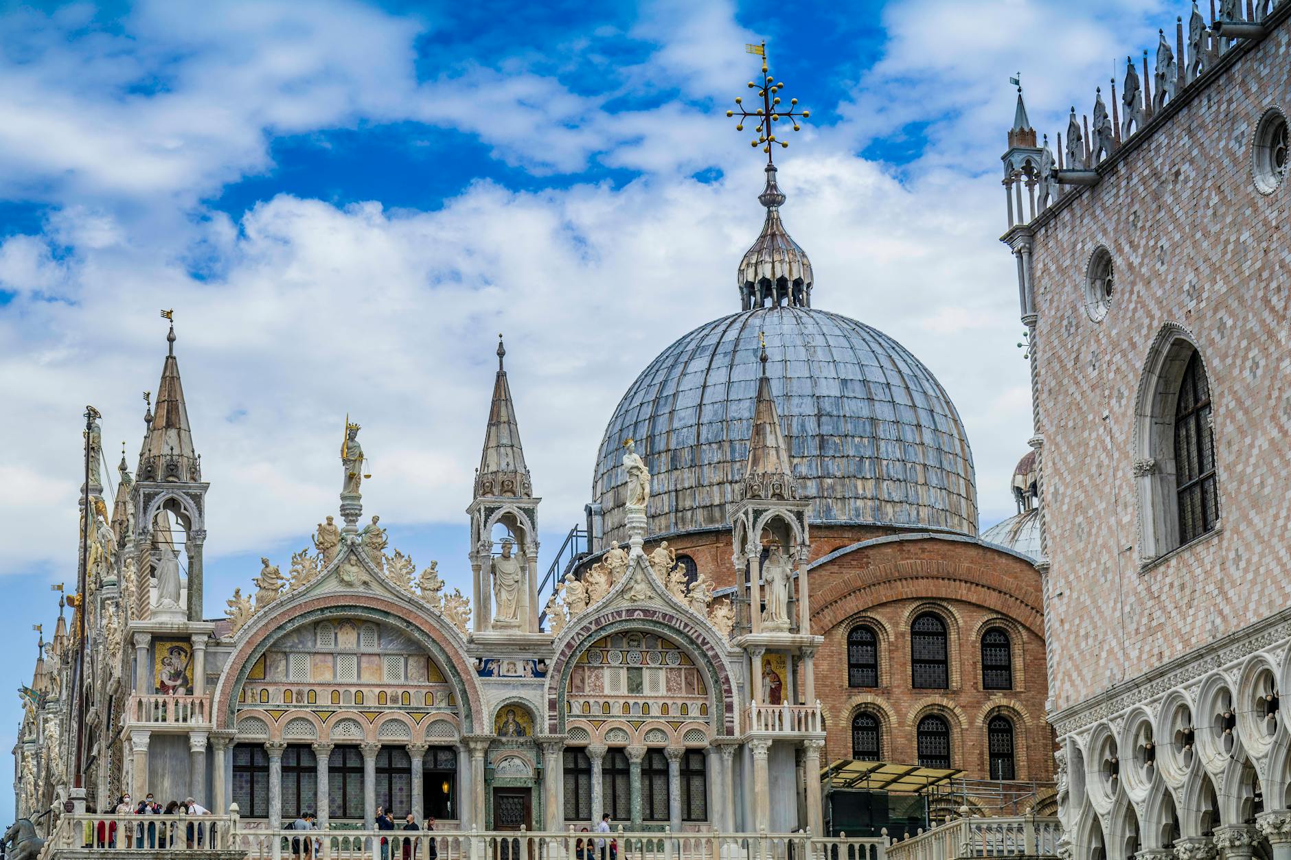 Facade of St. Mark's Basilica in Venice with ornate spires, statues, and a large dome under a partly cloudy sky