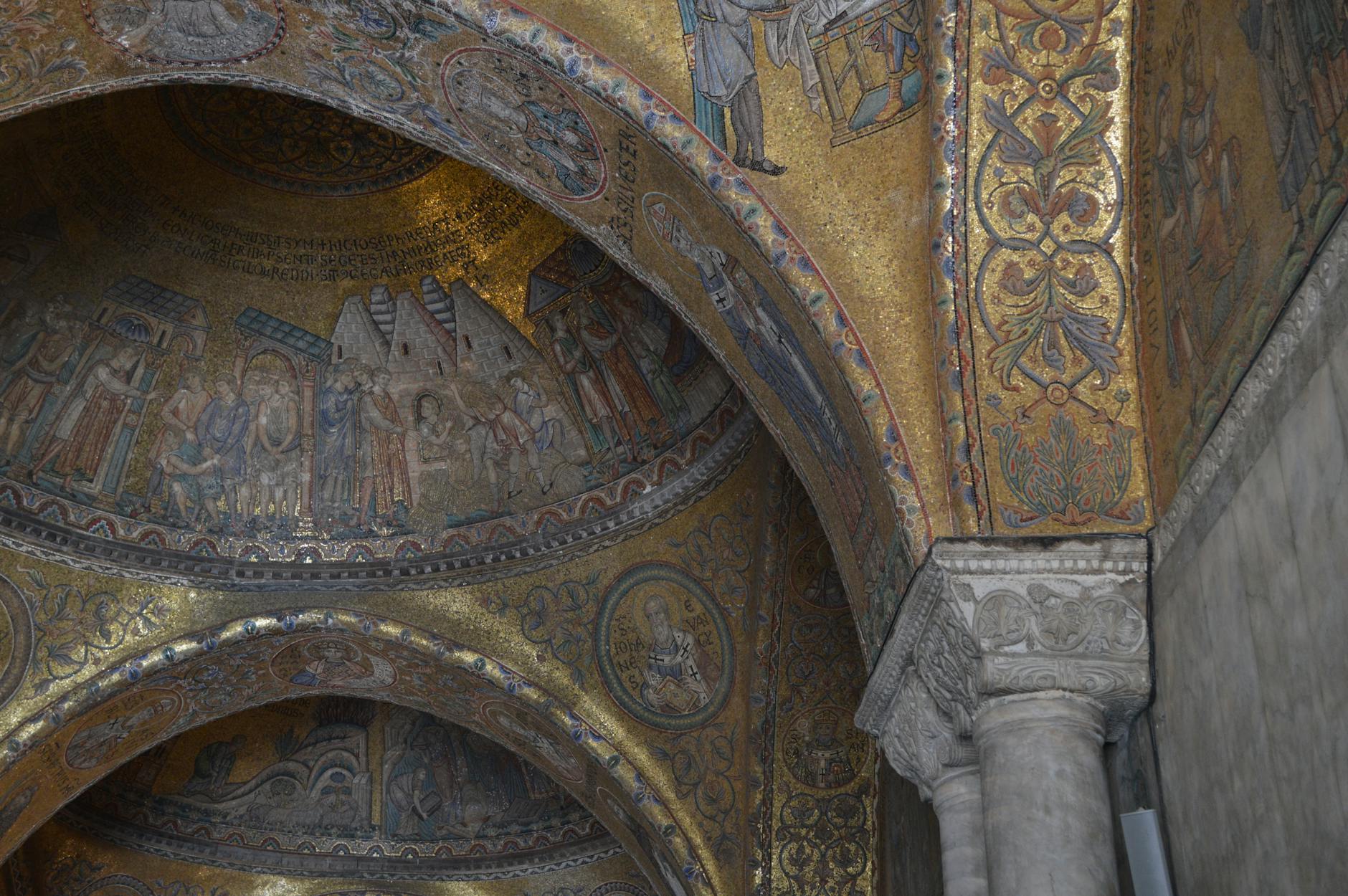 Mosaic ceiling with biblical scenes and saints framed by intricate gold and floral patterns above a marble column