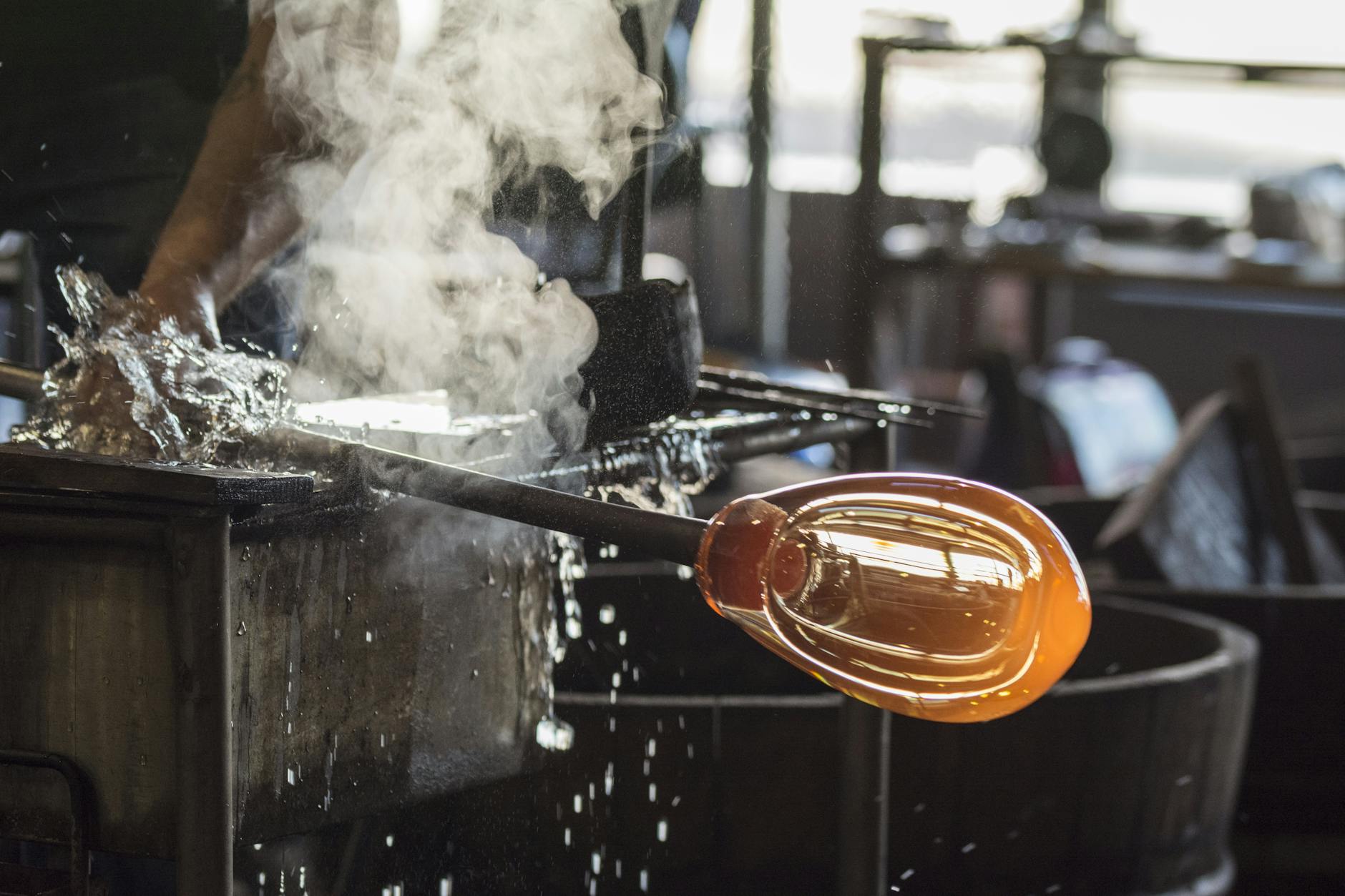 Molten glass being shaped at a glassblowing workshop with steam and water splashing