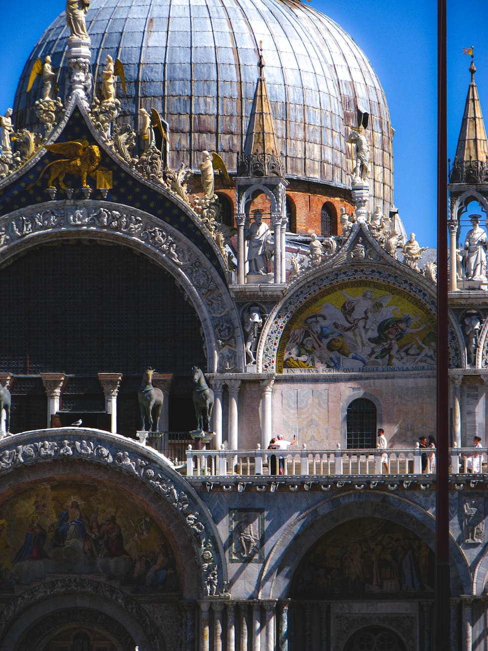 Facade of St. Mark's Basilica in Venice with detailed arches, statues, mosaics, and a large dome under a clear blue sky