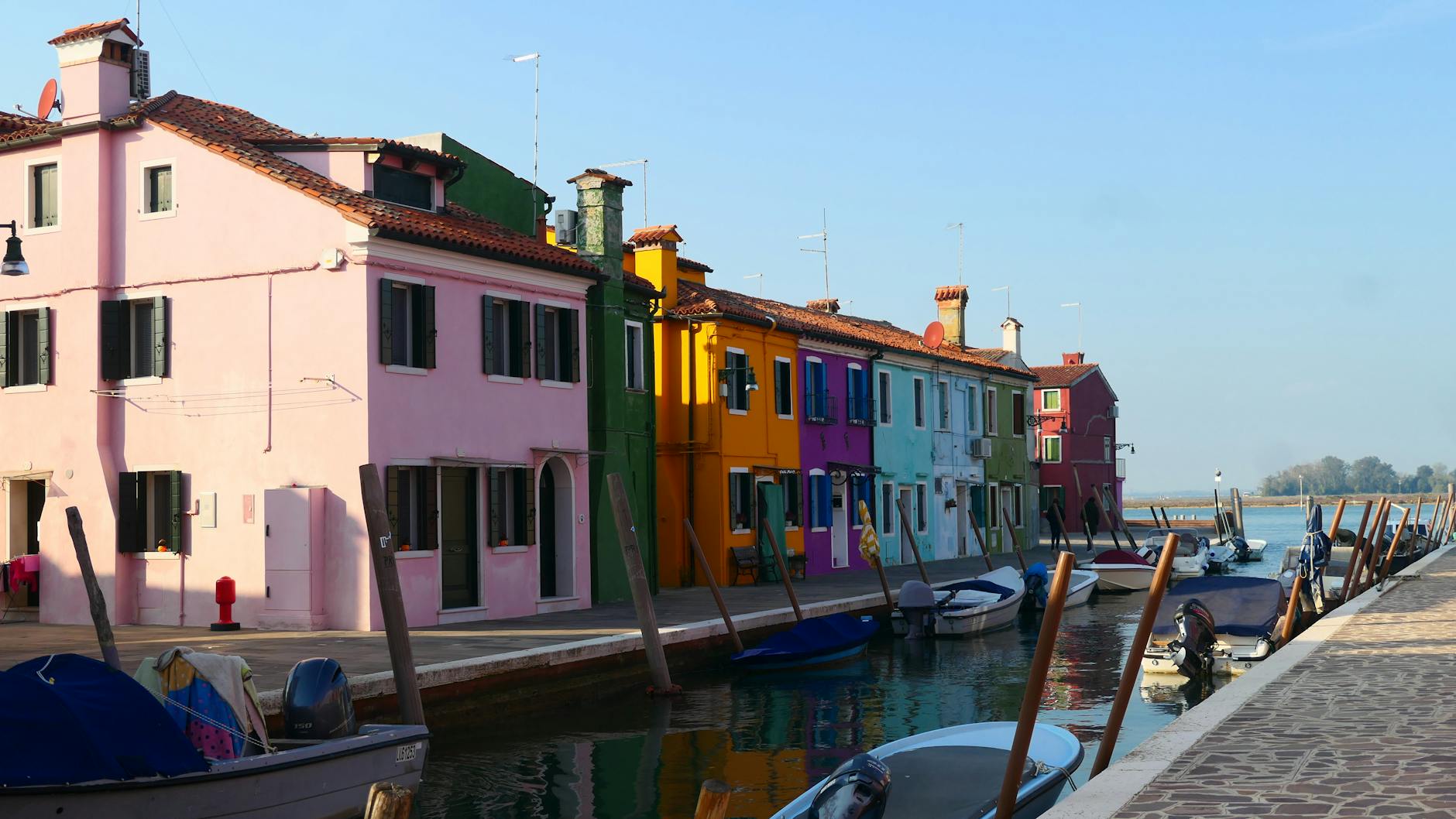 Colorful houses along a canal with small boats moored at the dock under a clear sky