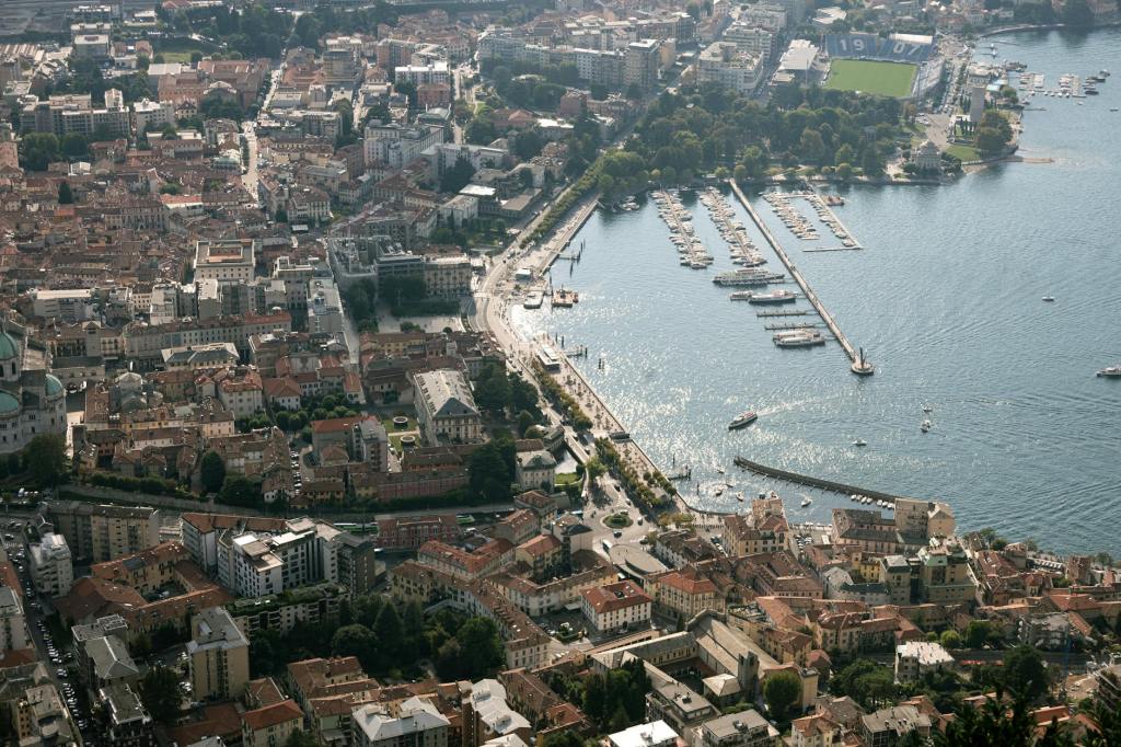 Aerial view of a lakeside city with marina, residential buildings, and green spaces, showcasing a bustling waterfront and organized layout.