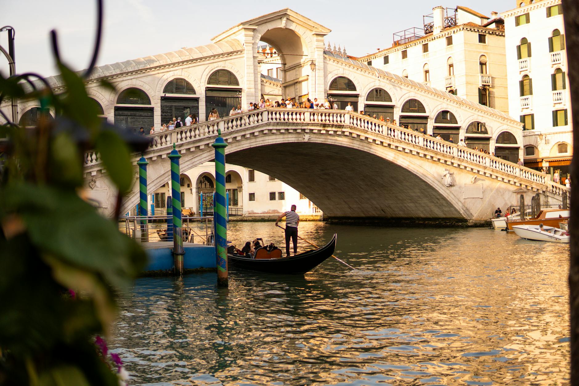 Rialto Bridge in Venice with tourists walking across and a gondolier steering a gondola on the canal below