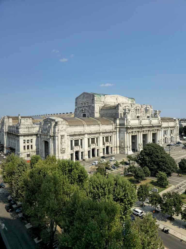 A view of a grand historical building surrounded by trees and clear blue skies, showcasing its architectural details.
