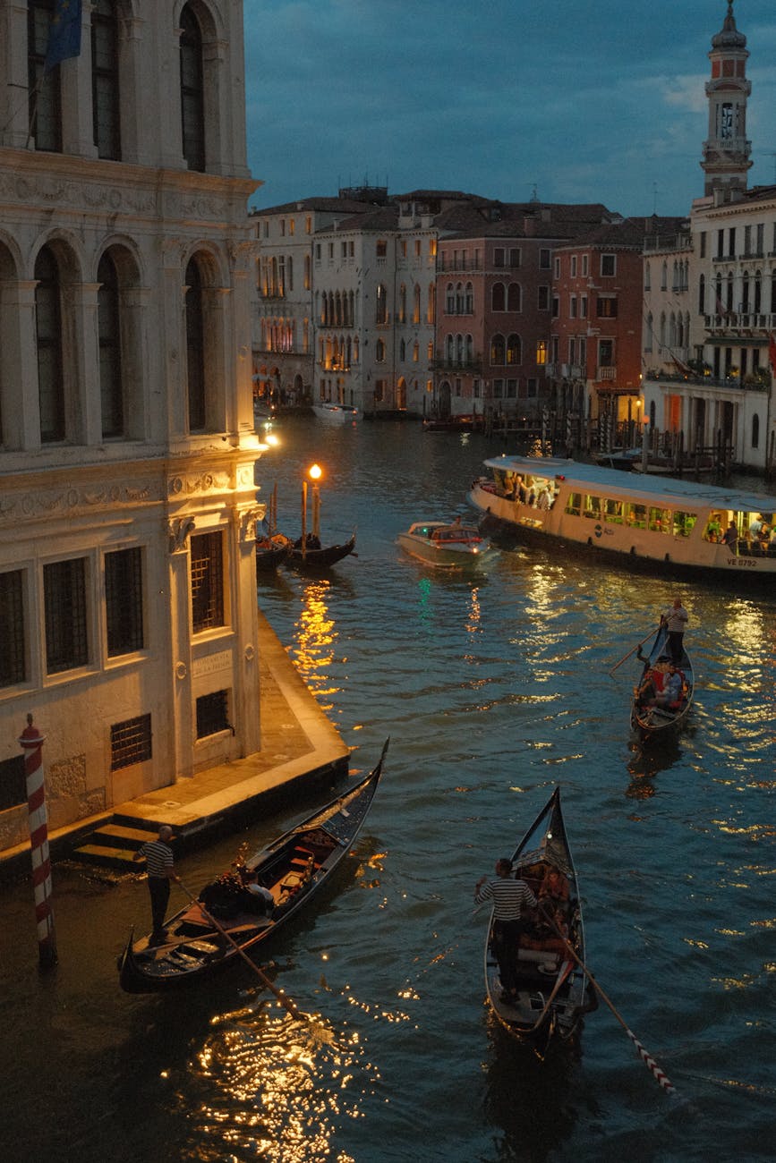 Evening view of gondolas and a vaporetto on a busy canal in Venice with illuminated historic buildings along the water