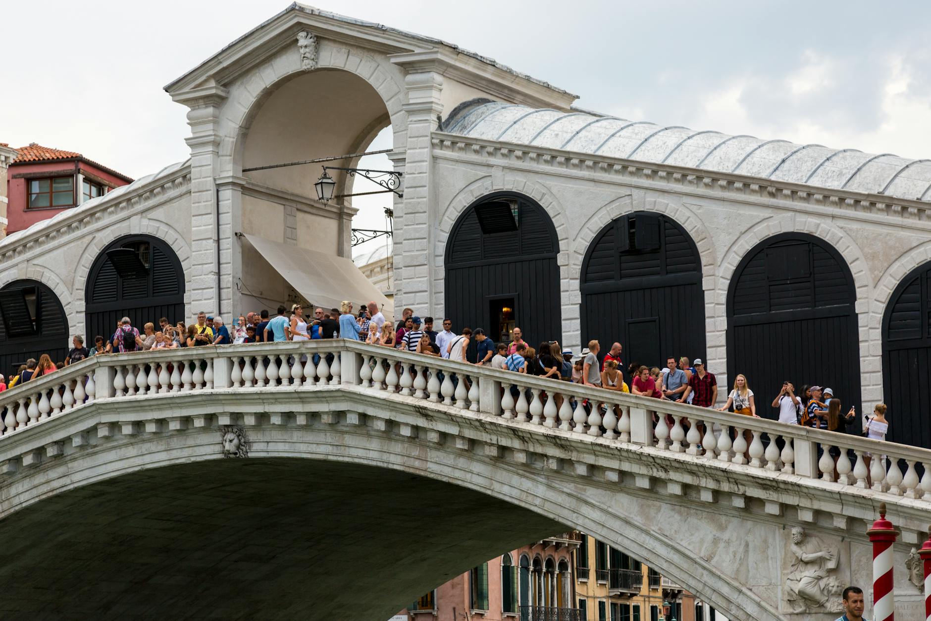 Crowds of people walking and standing on a historic white stone bridge with arched doorways and a covered walkway