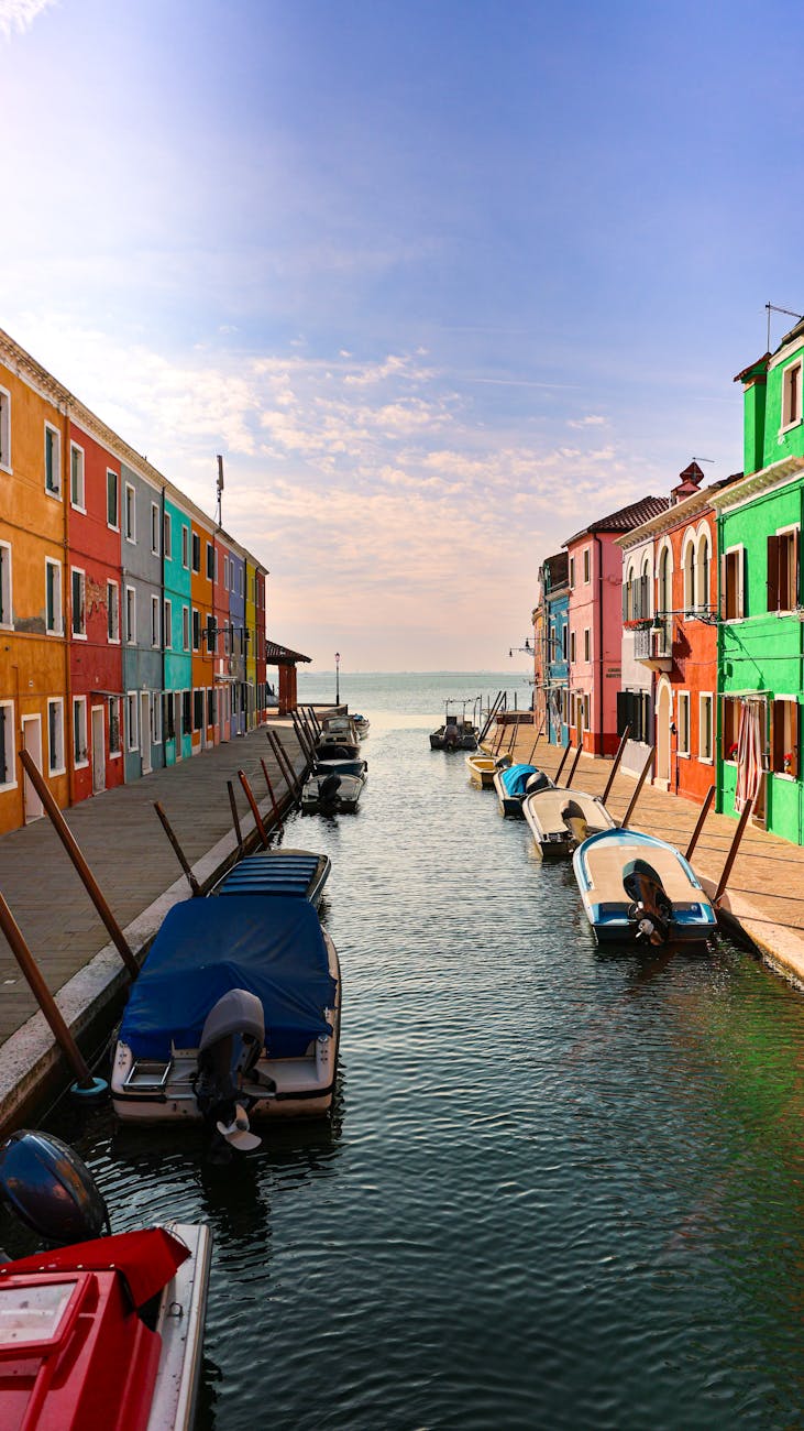 Canal lined with colorful buildings on both sides and small boats docked along the water under a partly cloudy sky