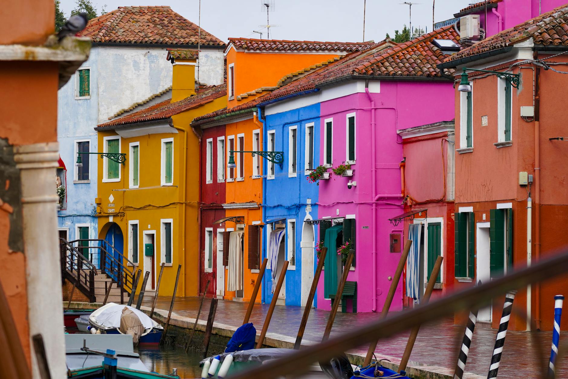 Colorful houses with red tiled roofs along a canal with boats docked in front