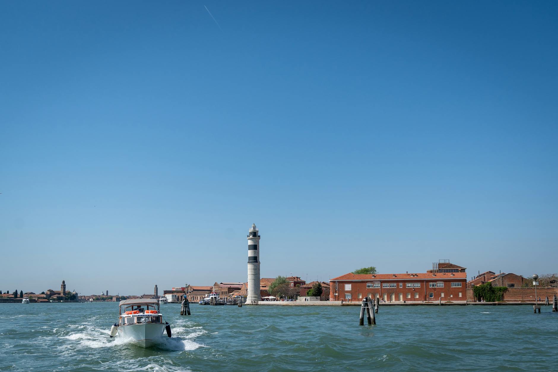 Motorboat moving on blue water near lighthouse and buildings under clear sky