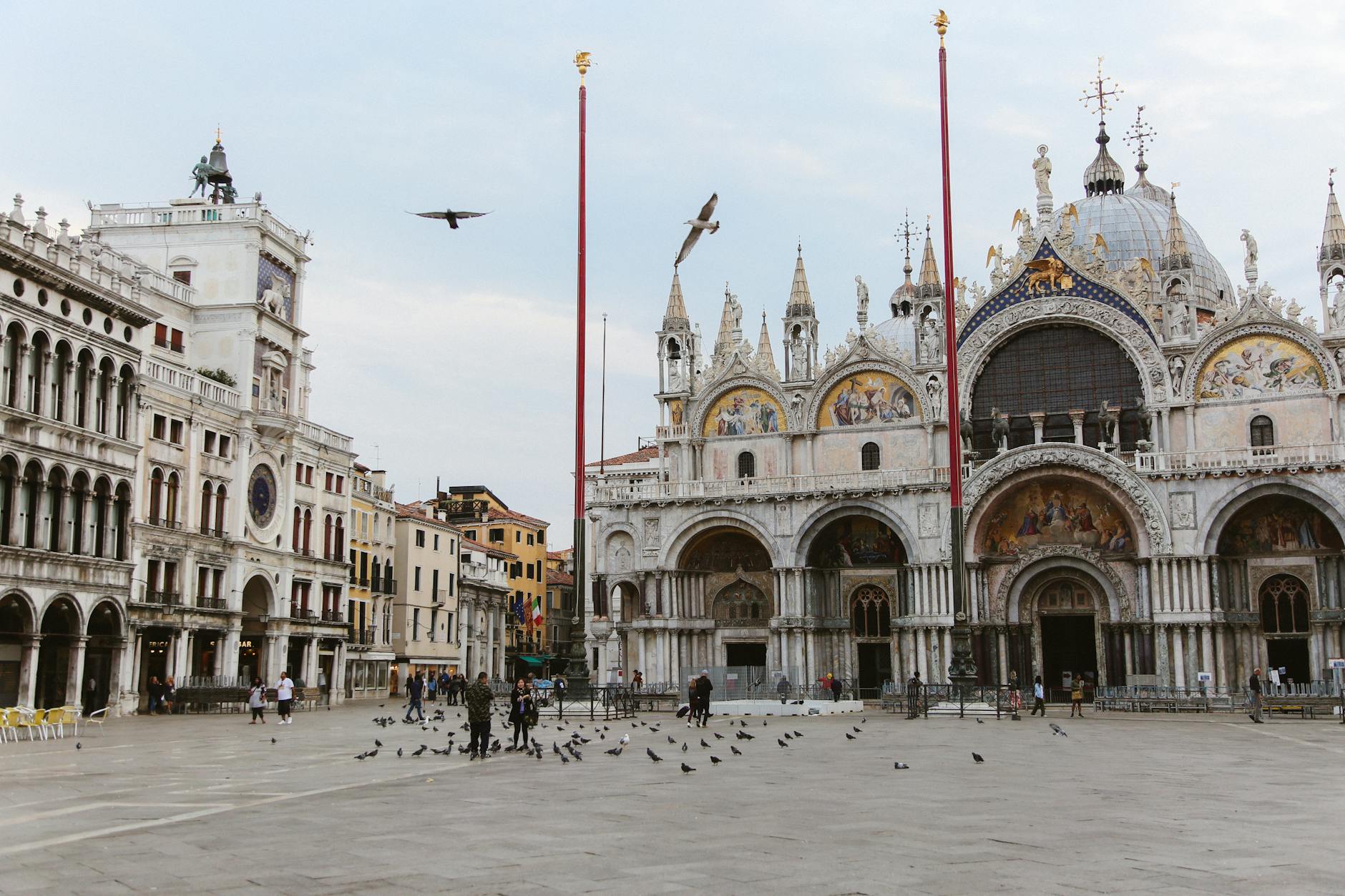 St. Mark's Basilica with detailed mosaics and sculptures in a historic square with birds and people.