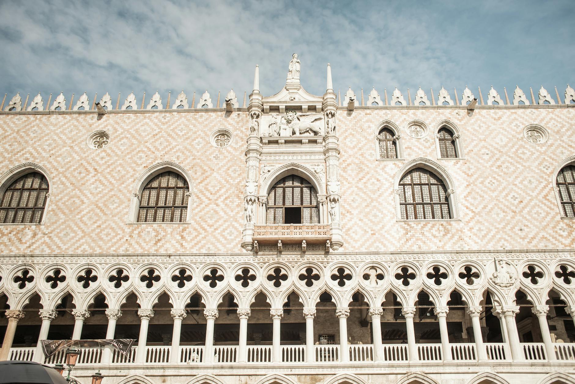 Ornate facade of a historic building with arched windows and detailed sculptures under a partly cloudy sky