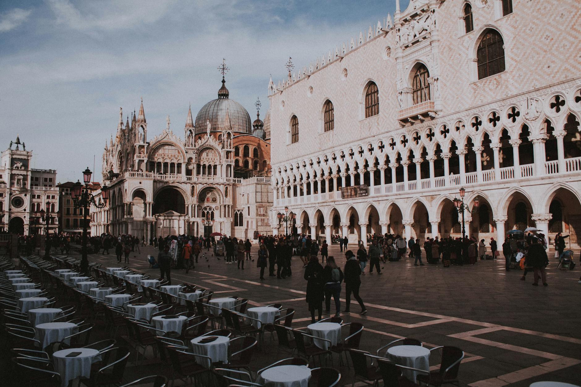 Crowded square with historic Venetian Gothic architecture and St Mark's Basilica dome