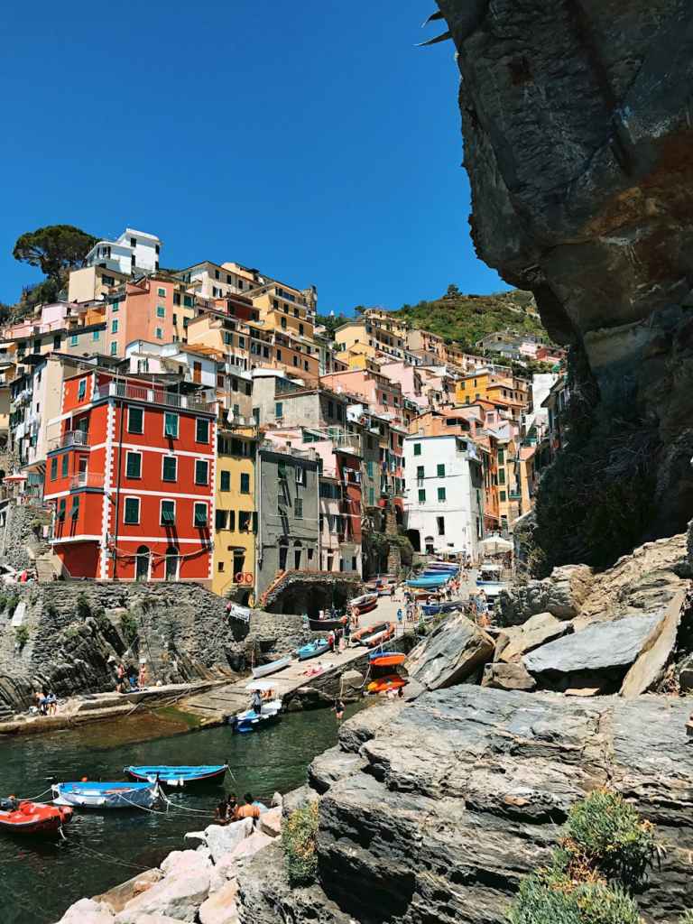 A picturesque coastal village with colorful buildings on a hillside, surrounded by rocky cliffs and a serene harbor filled with small boats.