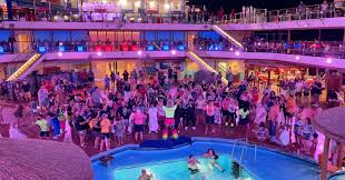 A lively pool deck party on a cruise ship, with a large crowd dressed in vibrant 1980s-themed outfits, dancing and celebrating under colorful lights.