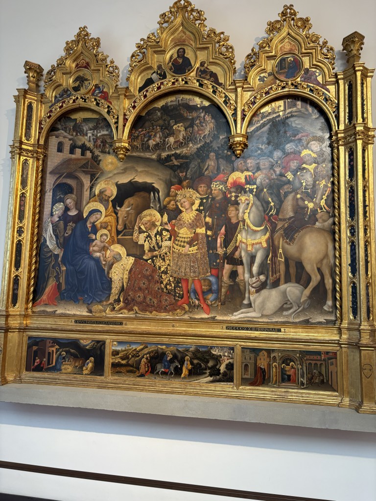 A detailed, ornate altarpiece depicting the Nativity scene. The artwork features Mary, Joseph, and baby Jesus surrounded by angels and a diverse group of figures, including kings and shepherds, in a richly decorated golden frame.