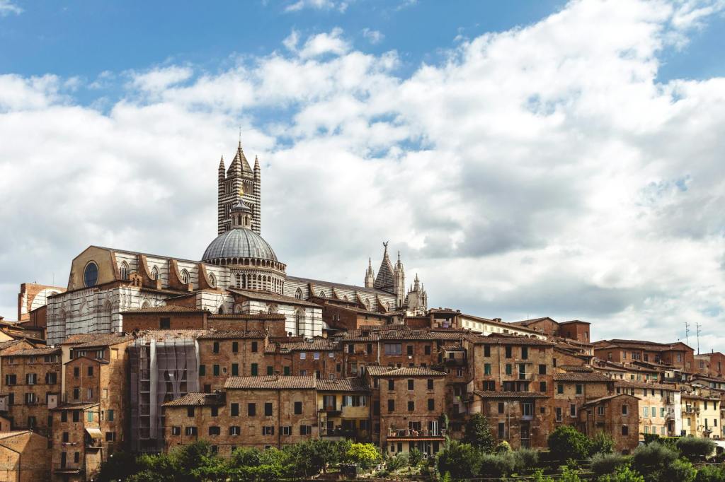 A panoramic view of historic buildings in Siena, Italy, showcasing the intricate architecture of the cathedral against a backdrop of cloudy skies.