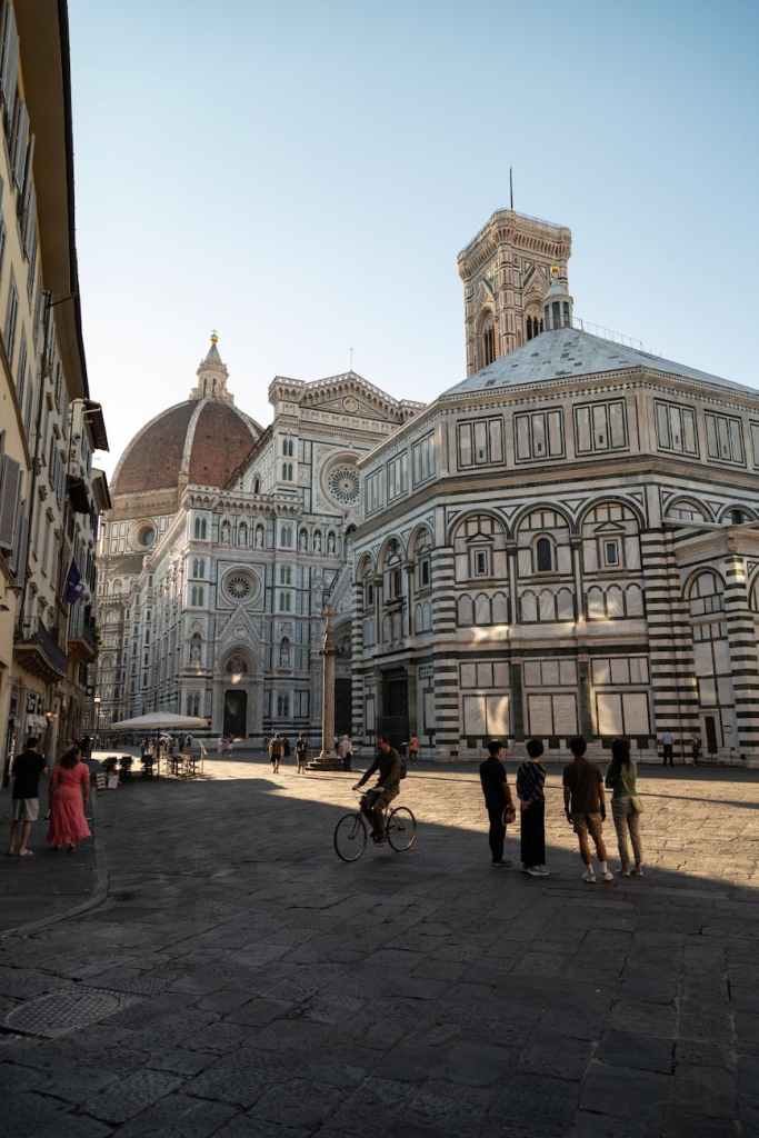 View of the Florence Cathedral and Baptistery in Florence, Italy, with street scenes showing pedestrians and a cyclist.