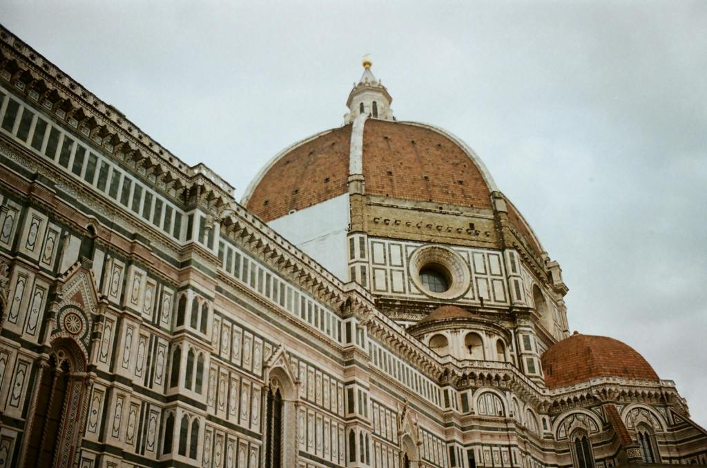 View of the dome of a historic cathedral, showcasing intricate architectural details and design elements against a cloudy sky.