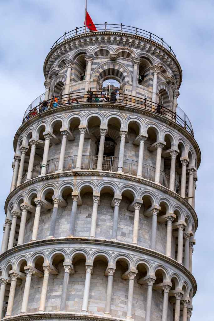 Close-up view of the Leaning Tower of Pisa, showcasing its distinctive arches and intricate architectural details against a cloudy sky.