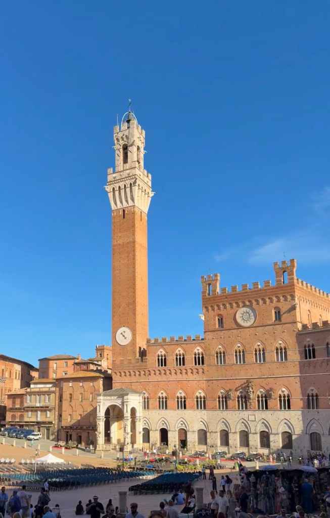 Piazza del Campo in Siena, Italy, featuring the Torre del Mangia tower and historic buildings under a clear blue sky.
