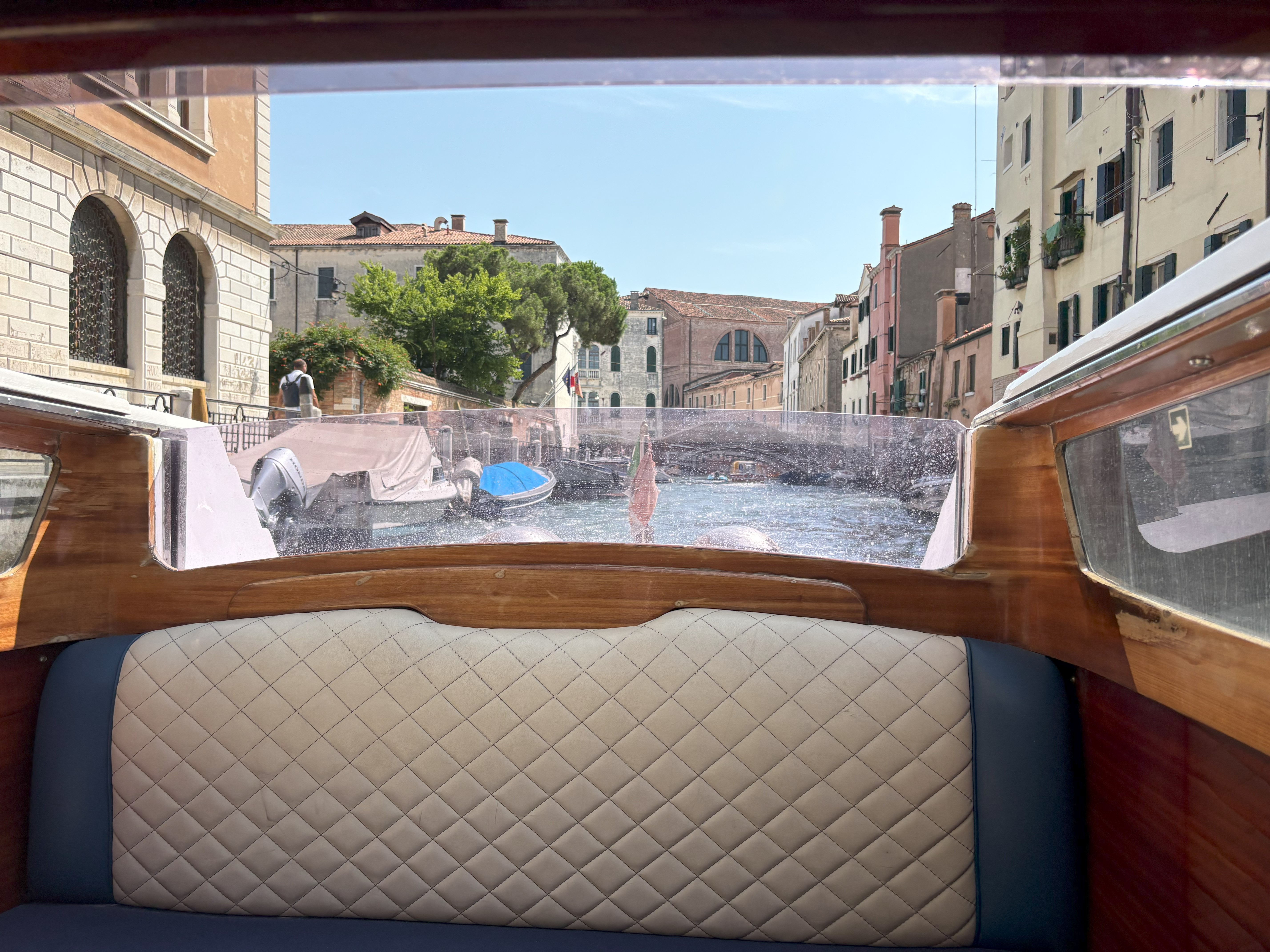 View of a canal lined with colorful buildings and boats from inside a wooden boat with a cushioned seat